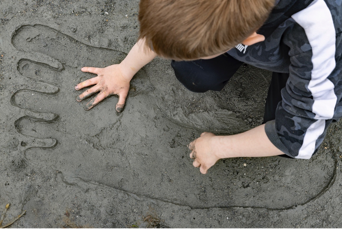 et kjempestor i sanden, en gutt legger hånden sin i sporet