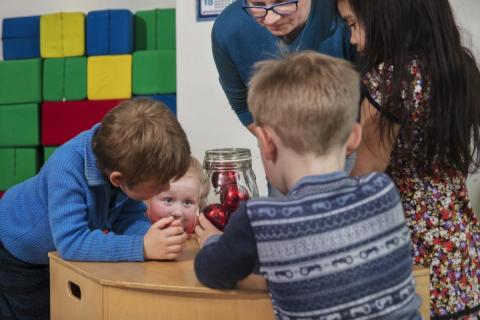 Barn og en voksen som ser på julekuler i ei glasskrukke
