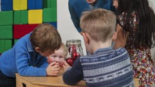 Barn og en voksen som ser på julekuler i ei glasskrukke